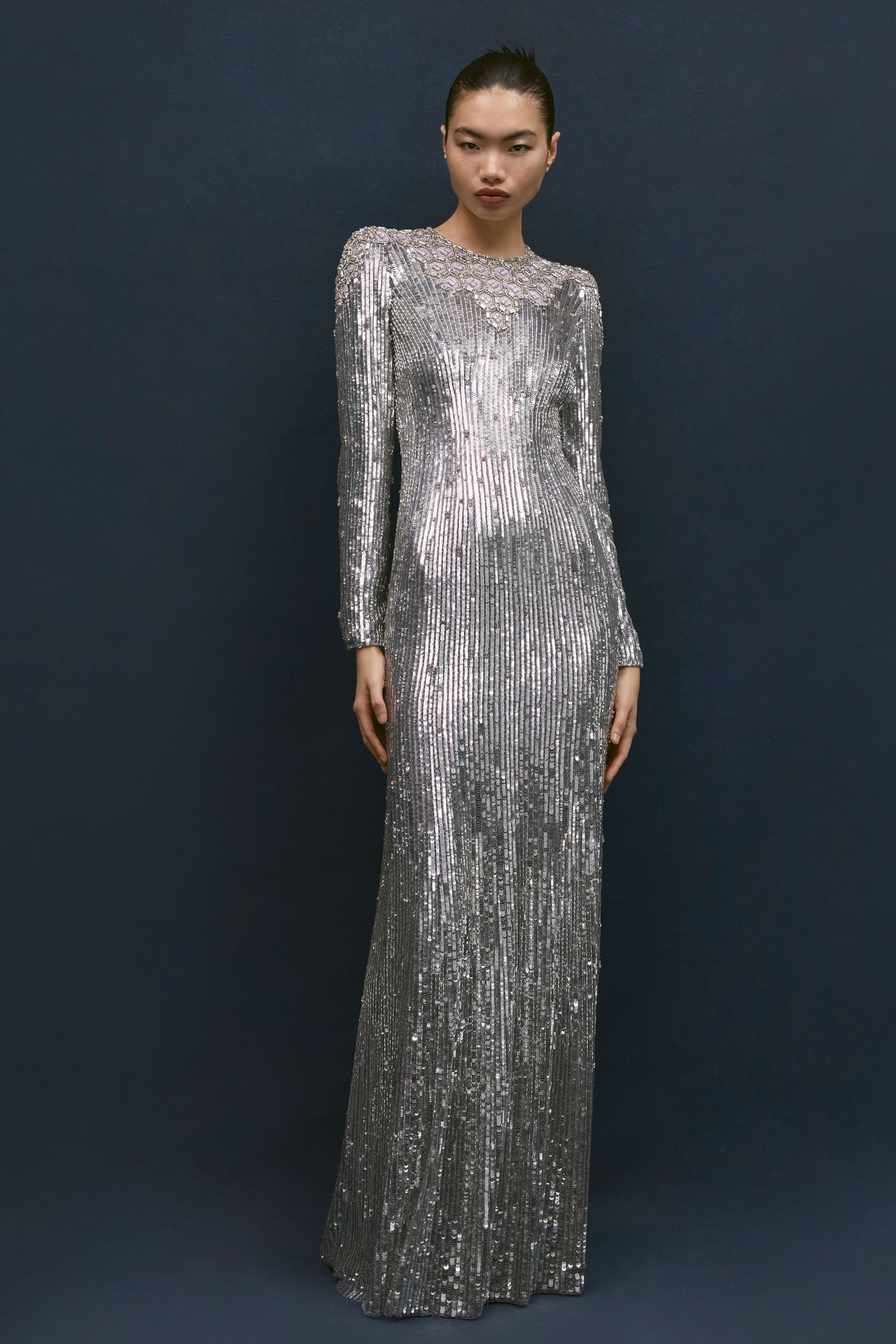Jenny Packham本季延续品牌标志性的红毯礼服风格，以闪耀流苏、金属光泽与修身长裙构建极具戏剧感的夜晚造型。银色亮片与深蓝礼服形成冷艳优雅的视觉对比，垂坠流苏与贴身剪裁让服装在行走间呈现波光般的流动感。设计在极简轮廓中加入华丽装饰，使整个系列既保留经典好莱坞 glamour，又展现现代女性的自信与优雅-顽石频道趋势研究